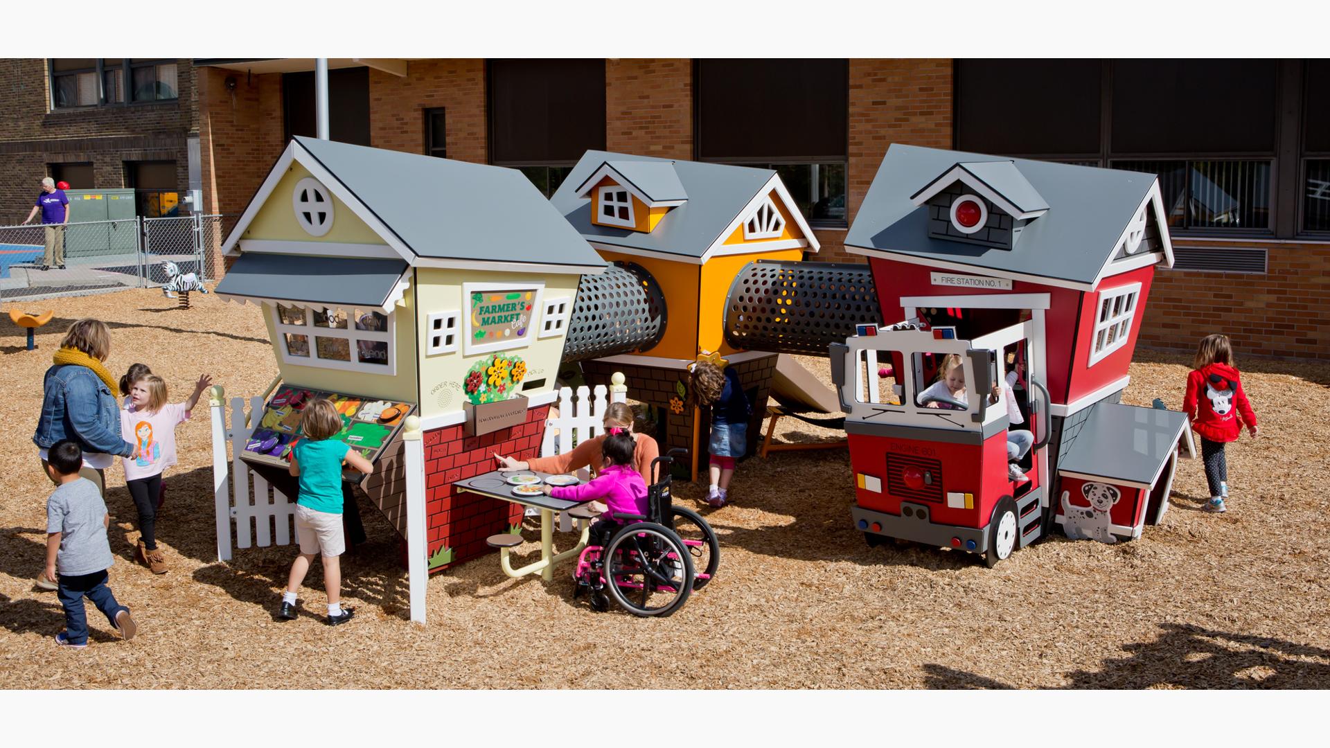 Young children and their parents play at the interactive connected play structures design as a market, small home, fire house and fire engine.